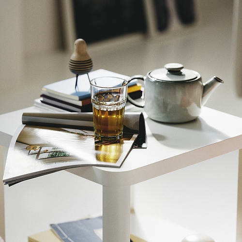 Un vaso de té encima de una revista sobre una mesa blanca, con una tetera de cerámica al lado.