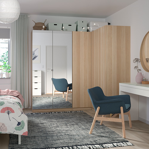 A modern bedroom a FORSAND light wood wardrobe, blue chair, and desk with sheer curtains allowing soft light in.