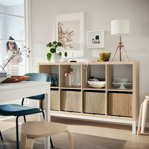 Salón moderno con estantería de madera KALLAX, sillas azules, lámpara y elementos decorativos.
