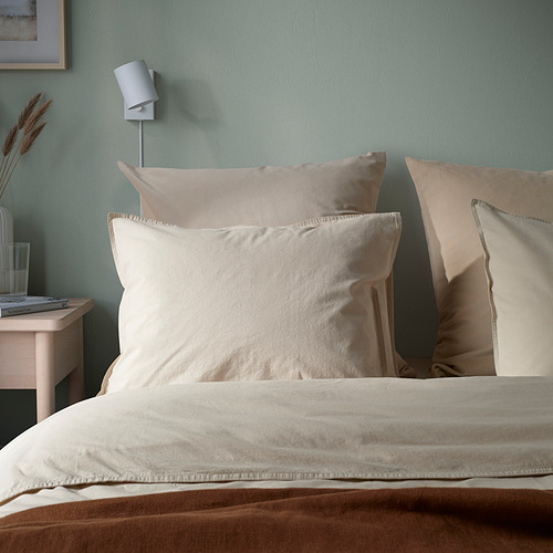 Cojín de terciopelo beige sobre la cama; suave, elegante con cremallera; Pared verde, luz blanca.