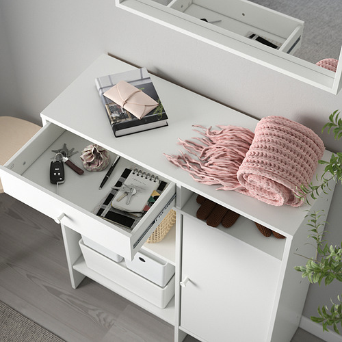 Mueble de almacenaje blanco con cajones y estantes, donde se exhiben libros, mandos a distancia y bufanda.