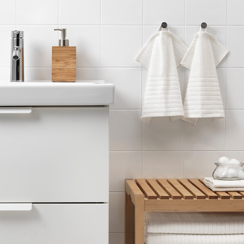 Baño moderno con toallas VÅGSJÖN en ganchos, toallero de madera y dispensador de jabón junto a grifo cromado.