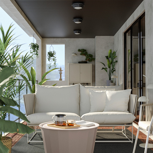 Moderno salón al aire libre con sofá HAVSTEN blanco, mesa de centro redonda blanca y exuberantes plantas verdes.