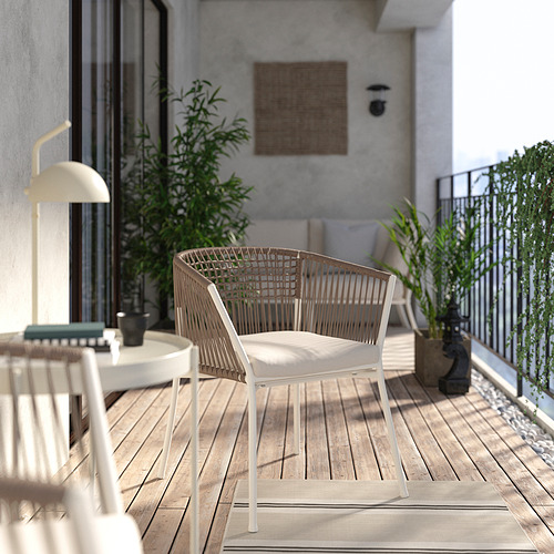 Balcón moderno con silla de mimbre SEGERÖN de color beige claro, mesa pequeña y plantas en macetas. Fondo de muro de hormigón.