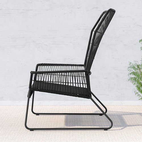 Silla de exterior de mimbre negro con respaldo y asiento curvos, colocada contra una pared clara. Diseño minimalista, cómodo para relajarse.
