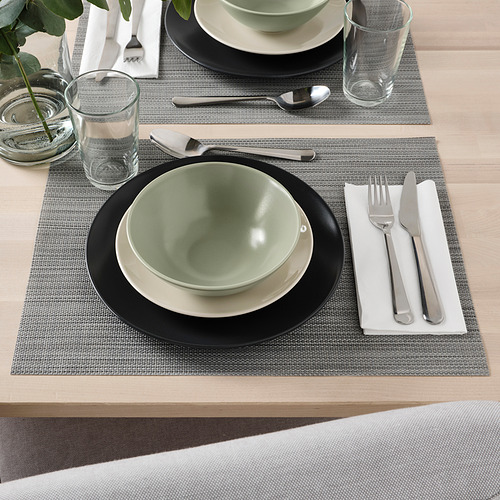 Conjunto de mesa con cuenco verde FÄRGKLAR, plato blanco, cubiertos, vaso sobre mantel individual tejido.