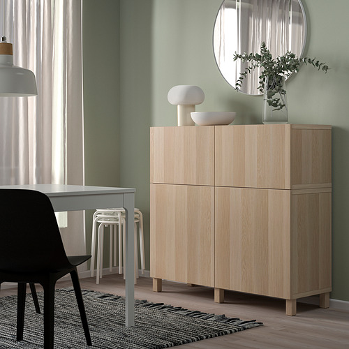 Light wood BESTÅ cabinet with doors in modern living space. Topped with vases and greenery. Its tall and narrow, fitting well under a round mirror.