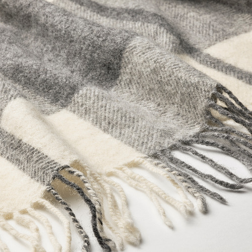 Primer plano de una acogedora manta de lana gris claro con una textura suave y cepillada y un tradicional estampado de cuadros. Los flecos son visibles a lo largo de los bordes.