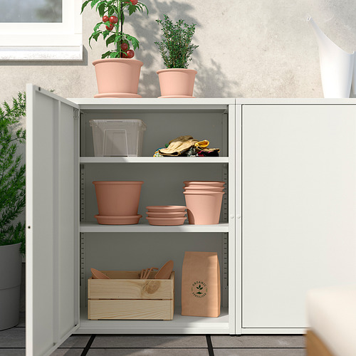 Mueble SUNDSÖ blanco con estantes ajustables que sostienen macetas de terracota naranja y herramientas de jardinería. Ideal para almacenamiento interior/exterior.