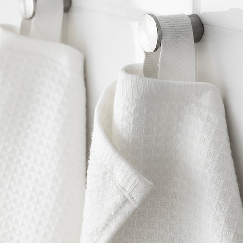 La toalla blanca con lado texturizado cuelga cuidadosamente en un gancho brillante: suave, absorbente, con detalles de calidad.