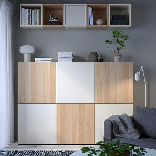 Sala de estar moderna con muebles de almacenamiento BESTÅ. Los estantes contienen libros, jarrones y plantas. El sofá, la lámpara y la alfombra completan el diseño minimalista.