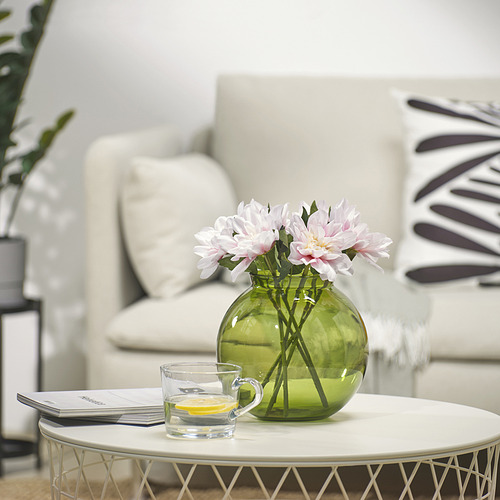 Pequeño jarrón verde con flores rosas en una mesa de centro redonda con taza de limón y revista.