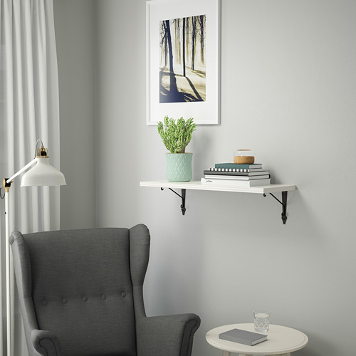 Sillón gris junto a mesita blanca. Estantería de pared con planta verde y libros. Impresión artística arriba.