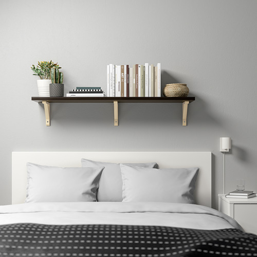 Dormitorio moderno con estante negro sobre la cama que muestra libros, canasta, cactus. Mesita de noche con lámpara y libros.