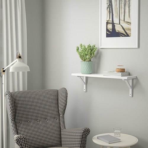 Sillón pata de gallo, estantería de pared blanca con libros y plantas, pared azul, cortina blanca y foto del bosque.