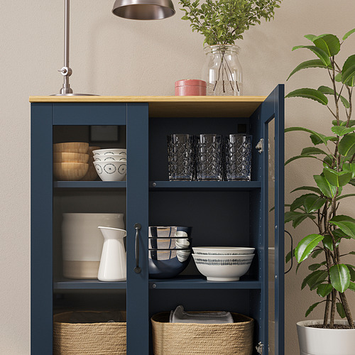 Gabinete azul con tapa de madera, puertas de vidrio, cuencos, vasos, jarrones y plantas.
