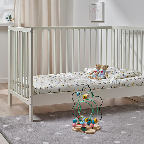 Cuna con osito de peluche y juguete de laberinto de cuentas de colores UPPSTÅ sobre alfombra.