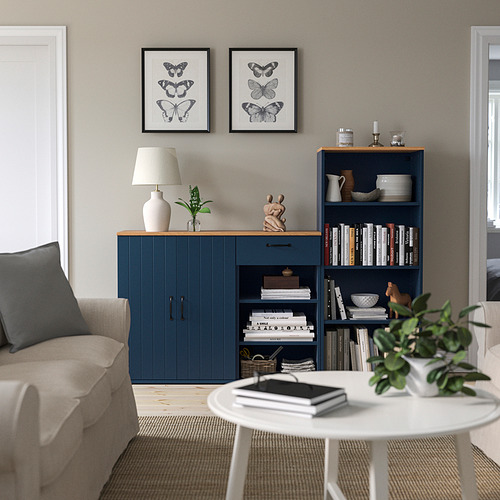 Sala de estar moderna con sofá beige, muebles SKRUVBY azules, libros, decoración, estampados de mariposas y una planta verde.