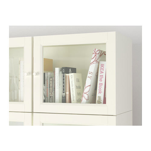 Librería BILLY blanca con puertas de cristal que exhiben libros, anclada a la pared, que ofrece protección contra el polvo.