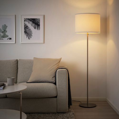 Moderno salón con lámpara de pie RINGSTA gris, pantalla blanca, junto a un gran sofá. La lámpara proporciona una luz suave y difusa.
