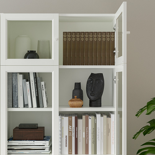 Librería blanca con estantes ajustables, donde se exhiben libros y artículos de decoración. Un estante tiene puertas de vidrio.