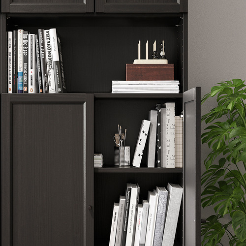 Librería negra con paneles de puerta ajustables, que alberga varios libros y artículos decorativos.