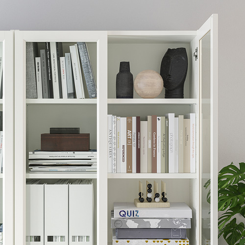 Librería blanca con estantes ajustables, algunas puertas de vidrio, que albergan varios libros y artículos decorativos.