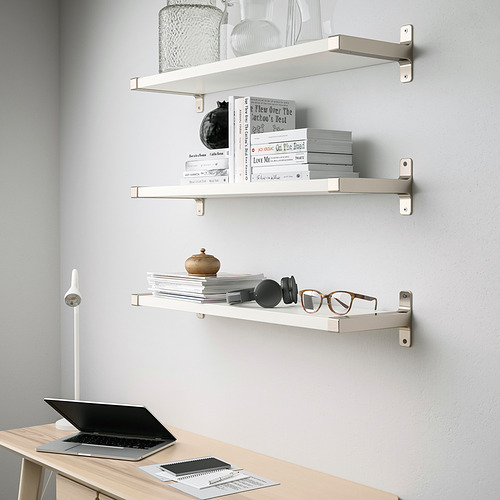 Tres estantes de pared blancos, cada uno con artículos decorativos y libros, instalados sobre un escritorio de madera clara con una computadora portátil y papeles.