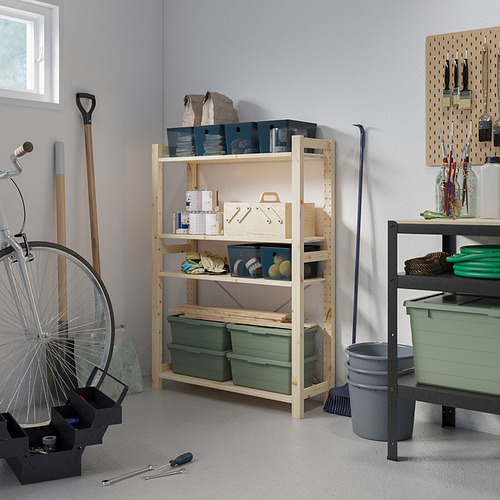 Un garaje con estanterías de madera IVAR que contienen herramientas y artículos. La gran estantería de color claro se mantiene erguida con contenedores verdes y otros artículos almacenados.