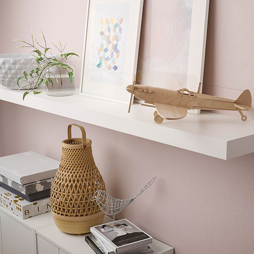 Un estante de pared que contiene artículos decorativos como un avión de madera, una cesta, libros y láminas de arte.