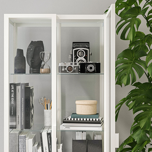 El armario con puerta de cristal MILSBO blanco exhibe y almacena los artículos de forma segura. Muestra objetos de colección y libros, con estantes ajustables.