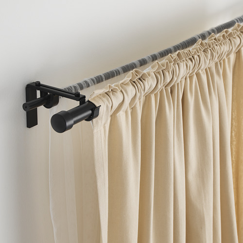 Barra de cortina negra que sostiene cortinas beige, longitud ajustable. Montado en la pared con soportes negros.