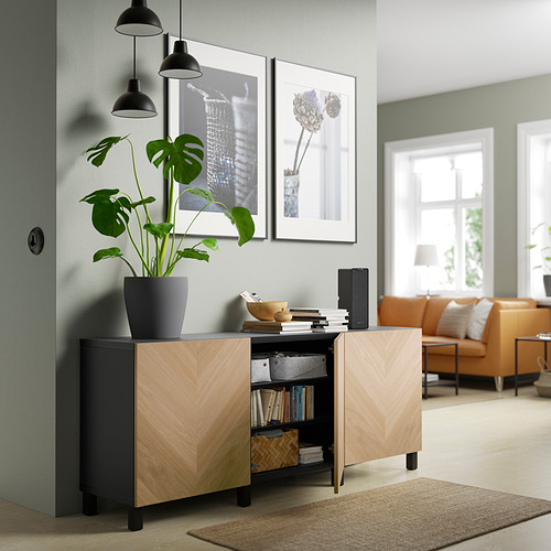 Modern living room with light wood BESTÅ sideboard, displaying books and plant, beneath framed art, next to orange seating area.