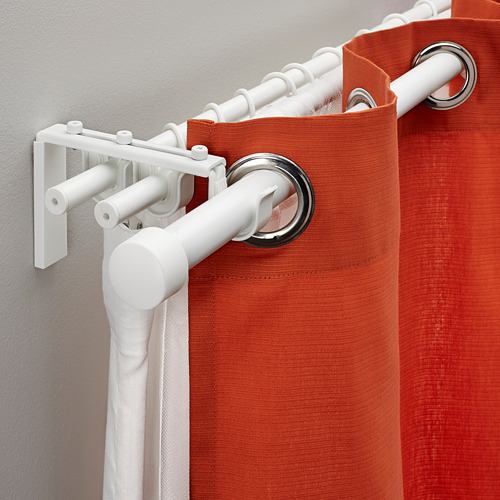 La barra de cortina triple blanca sostiene tres capas, como se ve montada en la pared con cortinas naranjas.