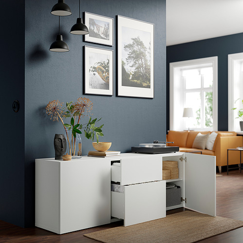 Salón moderno con aparador blanco BESTÅ. Tiene estantes ajustables y cajones con un jarrón y flores en la parte superior.