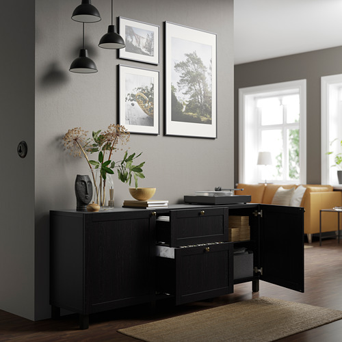 Black sideboard with open doors, shelves, drawers, decor, and lights. Framed pictures and window behind.