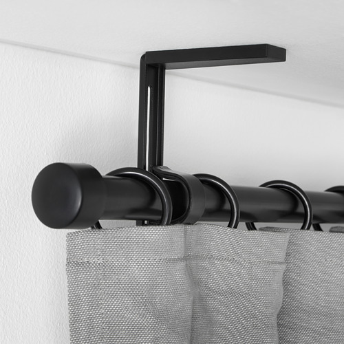 Soporte de barra de cortina ajustable negro que sostiene cortinas grises, montado en pared blanca.