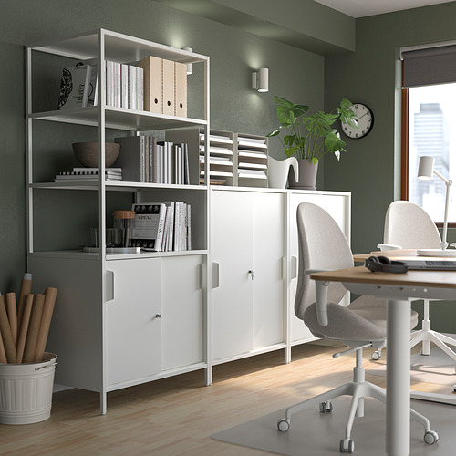 Oficina en casa moderna: armario blanco de doble cara con almacenamiento abierto y cerrado, decorado con plantas y libros. Silla gris sobre suelo de madera.