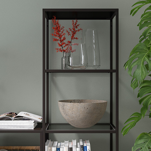 Moderno estante negro con paneles de vidrio que exhibe libros, jarrones y tazones. Se mantiene estable contra una pared, sosteniendo varios artículos ordenadamente.