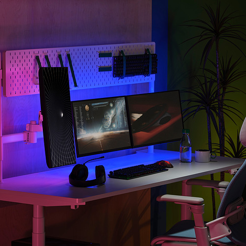 Modern desk with dual monitors, keyboard, mouse, gaming headset, and led lights. Pink office chair, spider plant, stylish workspace.