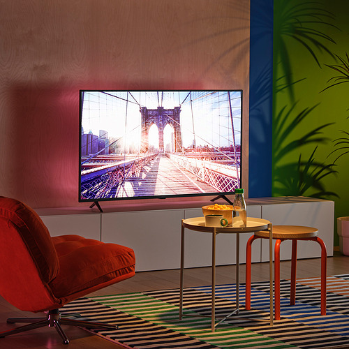 Modern tv room with colorful decor, large screen, orange chair, vibrant walls, led lighting, small table with snacks.