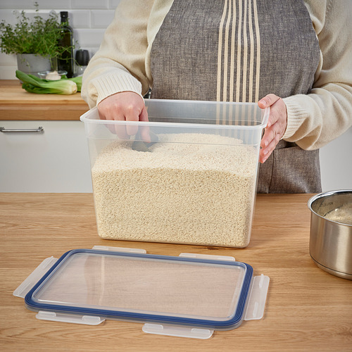 Persona sosteniendo un recipiente de arroz transparente, con la tapa cerca en el mostrador.