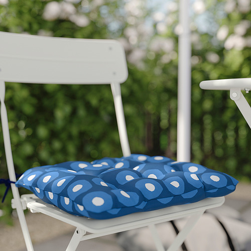 Cojín de asiento con estampado azul sobre silla de exterior blanca, sobre un fondo de follaje verde.