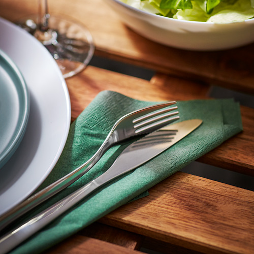 Juego de comedor de servilleta verde con cubiertos y platos sobre mesa de madera.