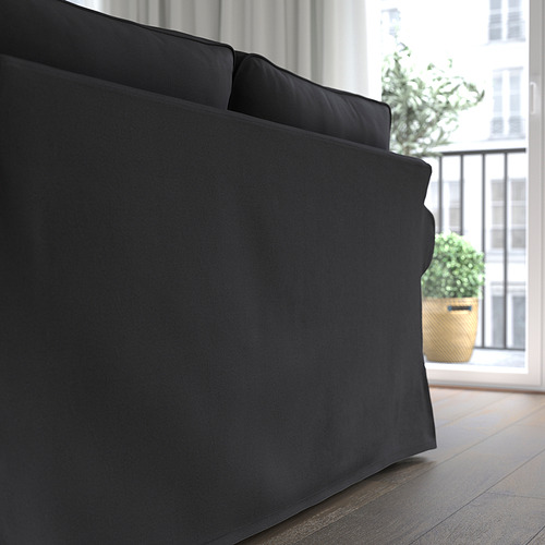 Moderno sofá negro con cojines suaves y reversibles cerca de una ventana con una planta.