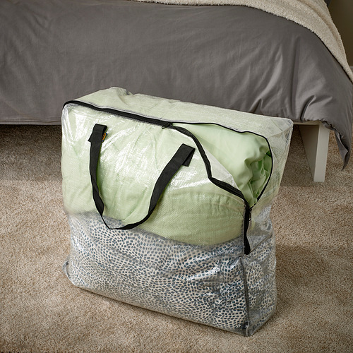 Bolsa de almacenamiento de plástico transparente con asas, descansa sobre una alfombra beige debajo de la cama.