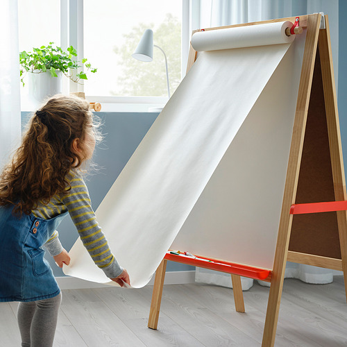 Un niño despliega un gran papel de dibujo de un caballete de madera con una pizarra y una pizarra blanca, promoviendo la creatividad y el aprendizaje.