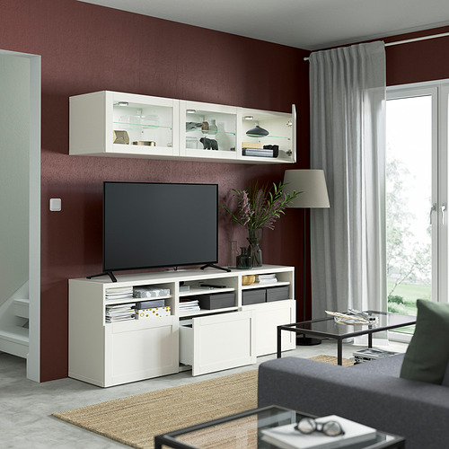 Sala de estar moderna con paredes granates, almacenamiento de televisores blancos BESTÅ, televisor de pantalla plana, gabinetes de vidrio y alfombra acogedora.