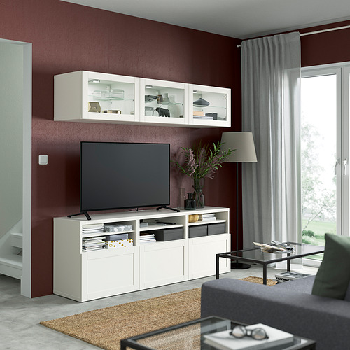 Sala de estar moderna con paredes granates, con un gran mueble de almacenamiento de TV blanco BESTÅ. Un sofá gris, una mesa de centro de cristal y una decoración completan el conjunto.