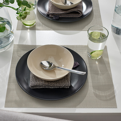 Mesa con cuencos beige, cucharas, platos negros, esteras grises y agua con cal.